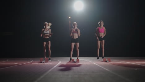 Front-view-Three-female-runners-prepare-to-run-in-a-dark-light-at-the-stadium-in-slow-motion